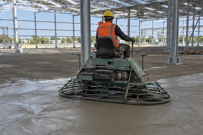 Operário operando alisadora mecânica helicóptero no acabamento de piso industrial de concreto fresco