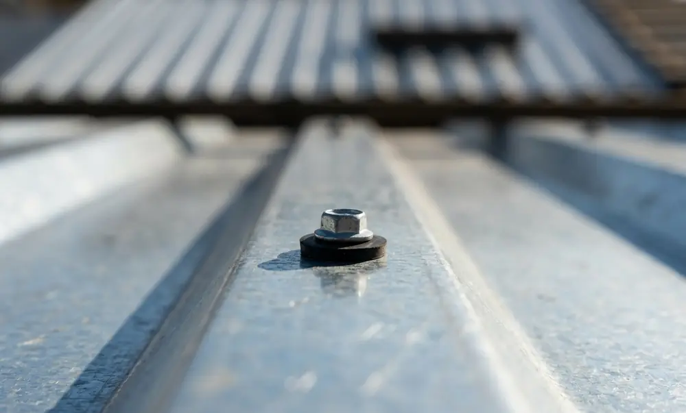 Parafuso autoperfurante com arruela EPDM fixando telha de zinco trapezoidal na crista da onda