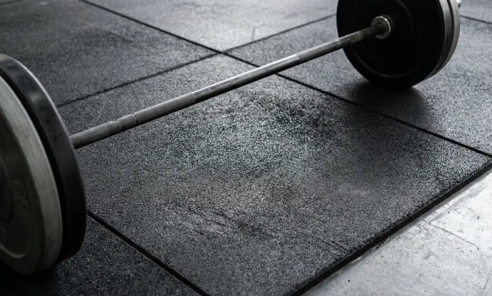 Piso emborrachado preto de alta densidade em box de CrossFit com barra olímpica e anilhas